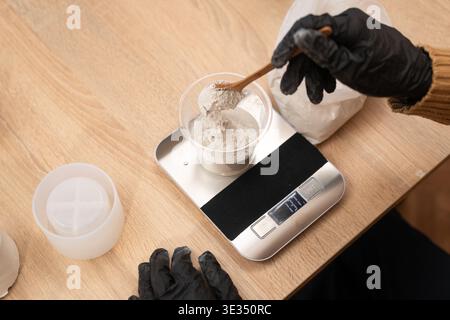 Close up of male hands in black gloves pouring dry gypsum powder into a cup on electronic scales. plaster for handmade candlestick production and DIY Stock Photo