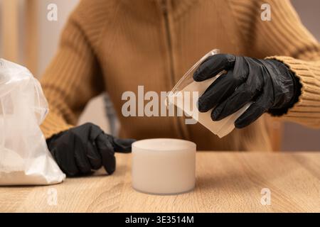 Craftsman in black gloves pouring liquid gypsum into silicone mold for candleholder. creating handmade decorative candleholders at home. Hobby and diy Stock Photo