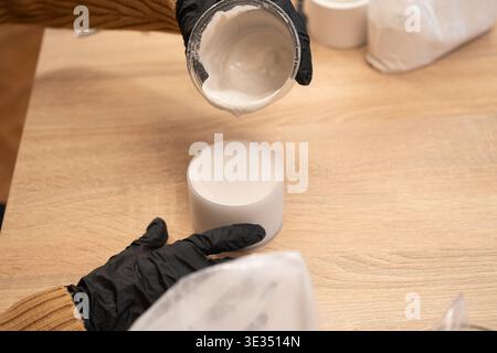 Craftsman in black gloves pouring liquid gypsum into silicone mold for candleholder. creating handmade decorative candleholders at home. Stock Photo