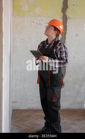 Woman builder or workman in orange hard hat using tablet pc computer. Building, renovation and technology concept Stock Photo