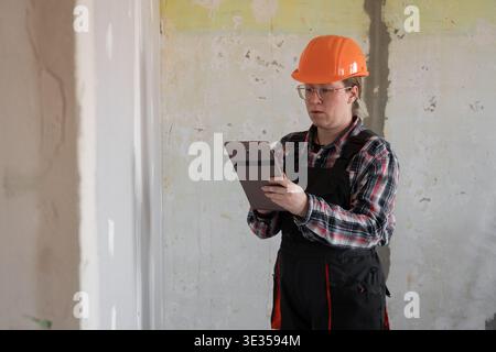 Woman builder or workman in orange hard hat using tablet pc computer. Building, renovation and technology concept Stock Photo