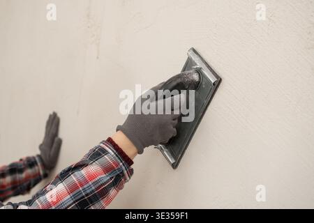 Construction worker using sandpaper for smoothing wall surface, finish during home renovation. close-up Stock Photo