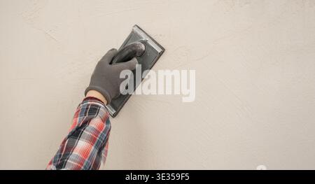 Construction worker using sandpaper for smoothing wall surface, finish during home renovation. close-up Stock Photo