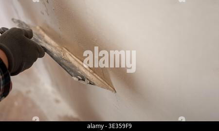 Professional builder applying white putty layer on wall surface during renovation. close-up Stock Photo
