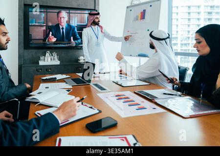 Multiethnic business professionals attending a corporate meeting in dubai, collaborating and presenting data while engaging in a video call with a rem Stock Photo