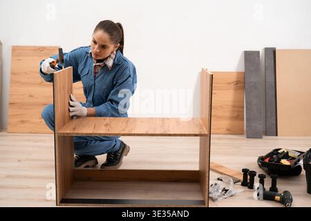 Professional furniture assembler installing wooden cabinets and cupboards in modern kitchen at home. Concept of furniture assembly. Stock Photo