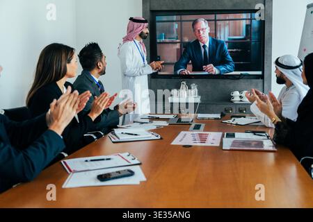Multiethnic corporate team members in dubai applauding a senior businessman on screen during a successful virtual video conference call, celebrating g Stock Photo