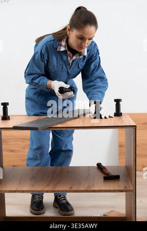 Woman worker installing furniture part during assembly cabinets using tools and plastic furniture legs. copy space Stock Photo