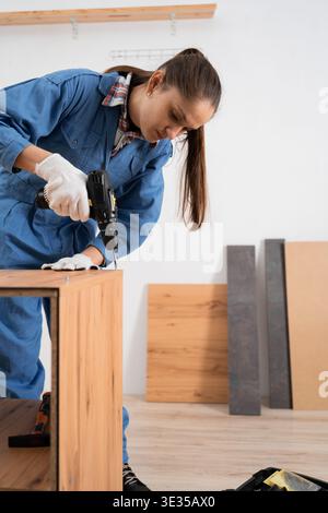Female craftsman assembles furniture using cordless drill. Installation and Furniture assembly. copy space Stock Photo