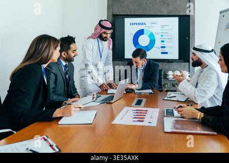 Multiethnic executives collaborate in a modern dubai office, reviewing financial data on a large screen and strategizing global business growth during Stock Photo