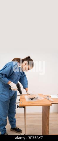 Female craftsman assembles furniture using cordless drill. Installation and Furniture assembly. vertical banner Stock Photo