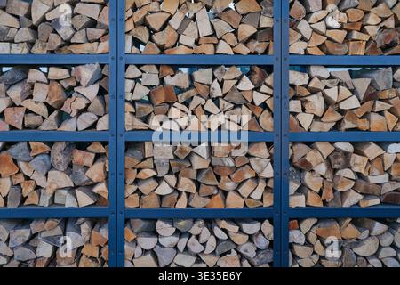 Stacked firewood arranged in a metal structure. Natural wood texture background with geometric pattern, rustic and organic material concept. Stock Photo
