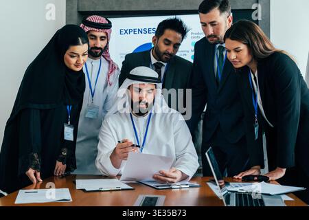 Multiethnic business team collaborating on financial data, analyzing expenses with diverse colleagues in a modern office meeting, fostering global par Stock Photo