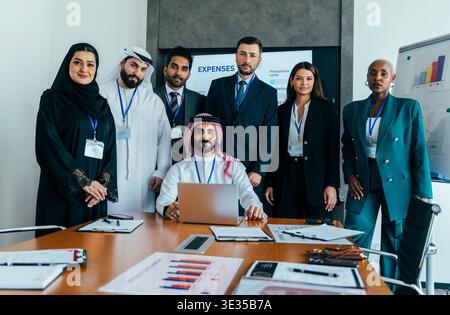 Multiethnic executive team in a modern dubai boardroom collaborating on finance strategies, reviewing charts and laptops to plan growth, investment an Stock Photo