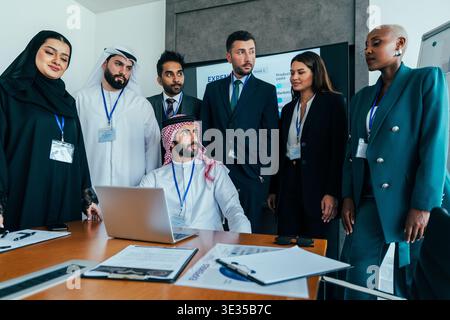 Diverse corporate professionals collaborating in a modern office, gathered around a table with a laptop and documents, engaging in a strategic busines Stock Photo
