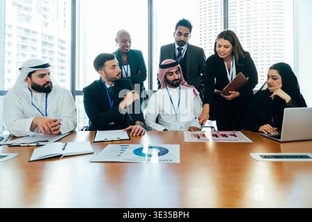 Multiethnic corporate team members collaborating and analyzing charts during a business meeting in a modern office with city skyscrapers visible throu Stock Photo