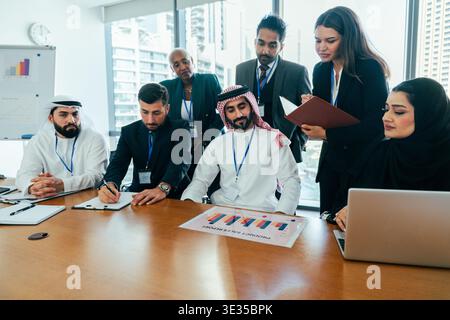 Diverse business professionals collaborating during an international corporate meeting, analyzing a product sales report on the conference table in a Stock Photo