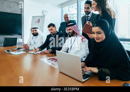Multiethnic business team collaborating during a corporate meeting in a modern office, using a laptop and discussing strategy for international busine Stock Photo