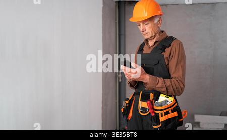 Focused Senior elderly builder using electric drill perforator during building construction or renovation. construction professional at work. Chatting Stock Photo