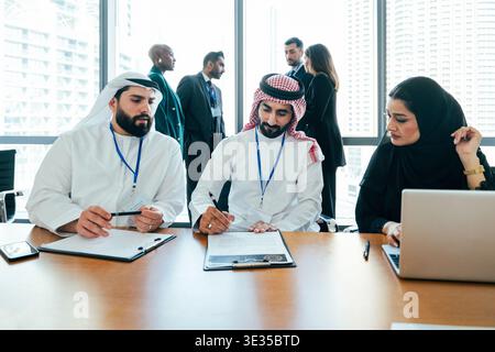 Multiethnic corporate business team meeting in a modern dubai office, two middle eastern male professionals signing a document while a female colleagu Stock Photo