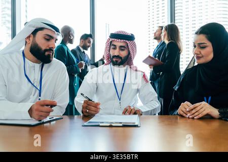 Group of diverse business professionals, including arab men and women, collaborating and discussing documents during an international corporate meetin Stock Photo