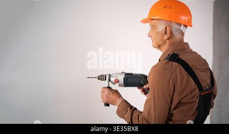 Focused Senior elderly builder using electric drill perforator during building construction or renovation. construction professional at work. banner Stock Photo
