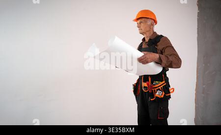 Focused Senior elderly builder holding paper blueprint or floor plan during building construction or renovation. construction professional at work. co Stock Photo
