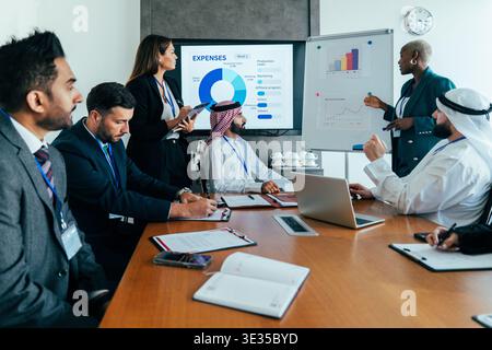 Multiethnic corporate team members collaborating during a business meeting in a modern dubai office, analyzing financial data and presentations on scr Stock Photo