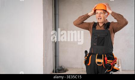 Tired sad builder or repairman senior man in safety helmet in stress on building site during renovation process. profession, construction and repair c Stock Photo