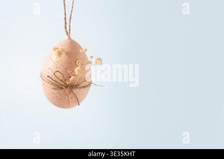 Minimal pastel Easter egg hanging on rope with dried flowers on soft gray background with copy space. Spring holiday decoration concept. Stock Photo