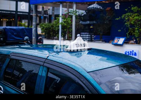 Blue Taksi Sign on Rain Covered Car Roof Stock Photo