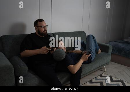 Young couple enjoying leisure time at home, a woman lying on a man's lap while both are focused on playing console video games, sharing a fun domestic Stock Photo