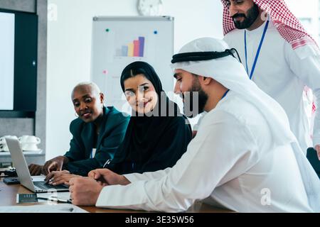 Multiethnic business professionals collaborating around a laptop during a corporate meeting in a modern office, discussing strategies and analyzing da Stock Photo