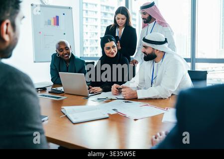 Diverse group of professionals collaborating and discussing ideas during an international corporate business meeting, leveraging technology and teamwo Stock Photo