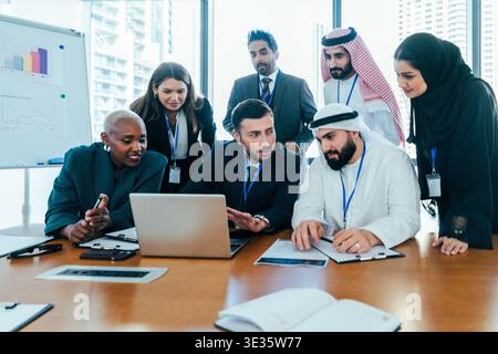 Multiethnic business people meeting in a modern office, discussing data and working collaboratively on a laptop, showing teamwork and global corporate Stock Photo
