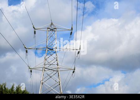 Low angle view of a steel electricity pylon rising into a partly cloudy sky, symbolising power, infrastructure and energy. Stock Photo