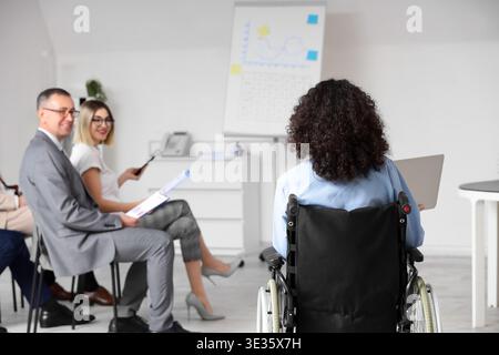 Group of people during seminar with business speaker in wheelchair at office, back view Stock Photo