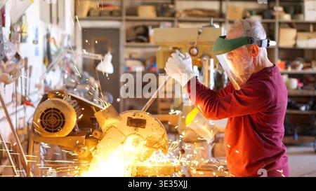 Senior metalworker cutting metal in workshop creating sparks Stock Photo