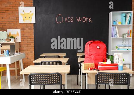 Emergency backpack, first aid kit and necessities on table in empty classroom Stock Photo