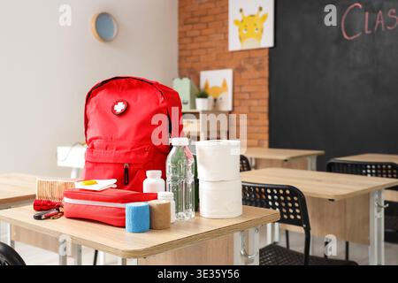 Emergency backpack, first aid kit and necessities on table in empty classroom Stock Photo