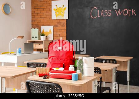 Emergency backpack, first aid kit and necessities on table in empty classroom Stock Photo