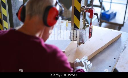 Woodworker cutting wood on band saw with ear protection Stock Photo