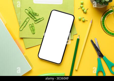Set of school stationery with mobile phone and houseplant on yellow background Stock Photo