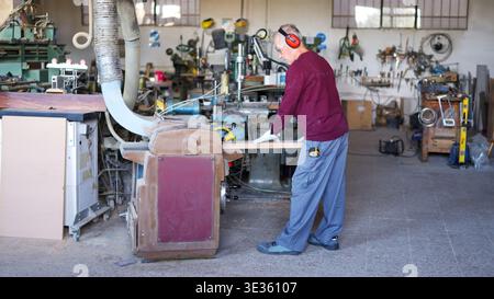 Elderly man working wood plank with a thicknesser in workshop Stock Photo