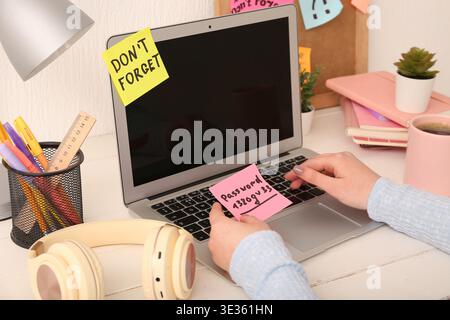 Woman with written password and laptop on white wooden table, closeup Stock Photo