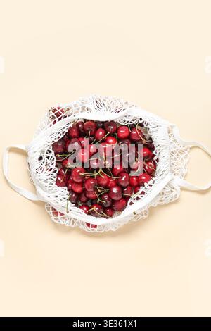 Mesh bag with fresh cherry on beige background Stock Photo