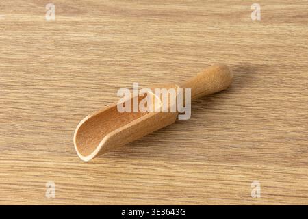 A single, empty wooden scoop placed on a flat wooden surface. The scoop is made of light-colored wood with a visible grain, featuring a rounded handle Stock Photo