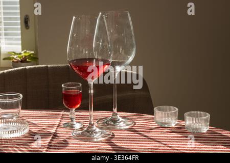 Elegant wine glasses with red wine placed on a striped tablecloth in warm afternoon light. Intimate dining scene with soft shadows and glass reflectio Stock Photo