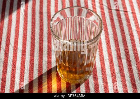 A glass of tea sits on a red and white striped tablecloth, catching sunlight in a bright, natural setting Stock Photo