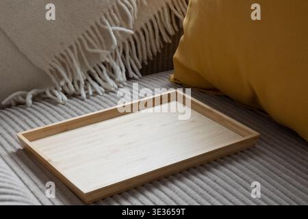 A rectangular light-colored bamboo tray sits empty on the ribbed surface of a gray corduroy sofa. To the right, a vibrant yellow pillow adds a pop of Stock Photo